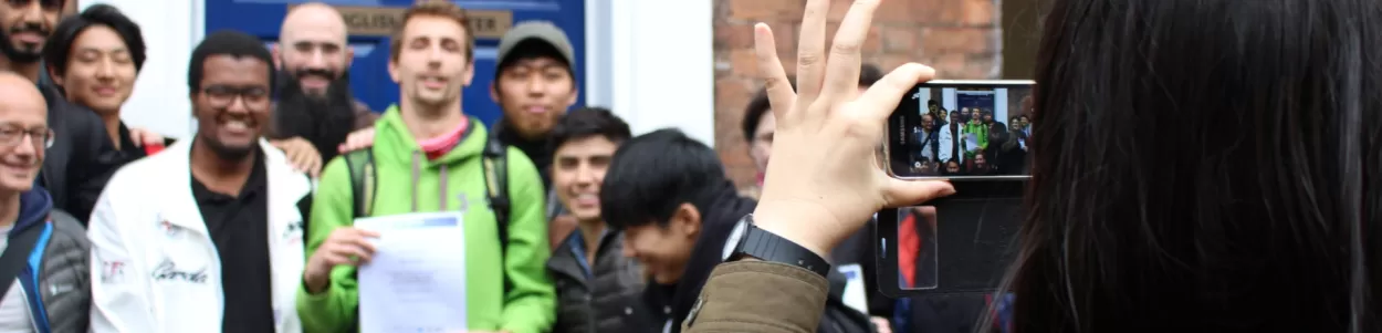 A heavily cropped image showing a student taking a photo of other students holding their end of course certificates, having finished their English language programme at the English language centre in Chester.