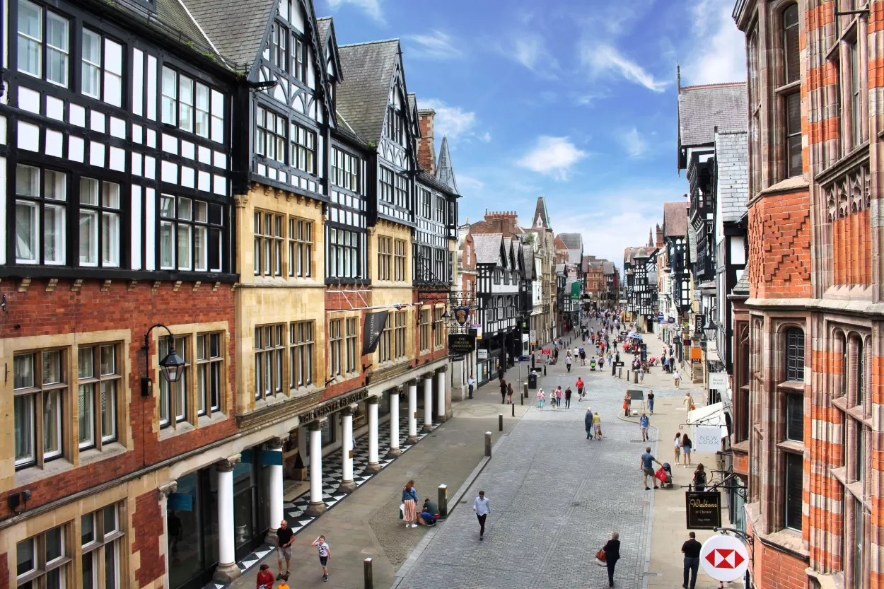 A professional photograph of one of the main streets in Chester which shows the mock Tudor buildings with the walkway underneath. The street appears to disappears off into the distance due to the perspective.