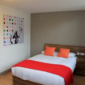 A double bed in the Britannia Student Residence in Brighton. There are orange cushions on the bed and a brighter orange blanket across the foot of the bed.
