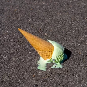 A photo of mint coloured ice cream which has been dropped onto the tarmac. The ice cream has begun to melt.