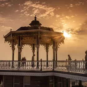 A late evening photo of the bandstand on the seafront in Brighton. The structure has been totally renovated and the detailed iron work is partly silhouetted against the sky.