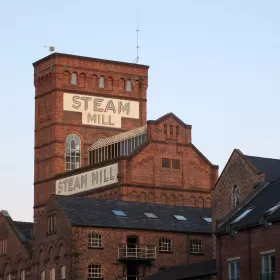 A photo of the Steam Mill in Chester which was built in 1786, orginally to mill corn and flour. The building is a prominent red brick building with lots of roofs at different angles.