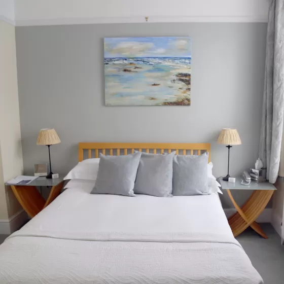 A photo of a double bed at the Claremont Hotel in Brighton. There is a painting of the sea above the bed.