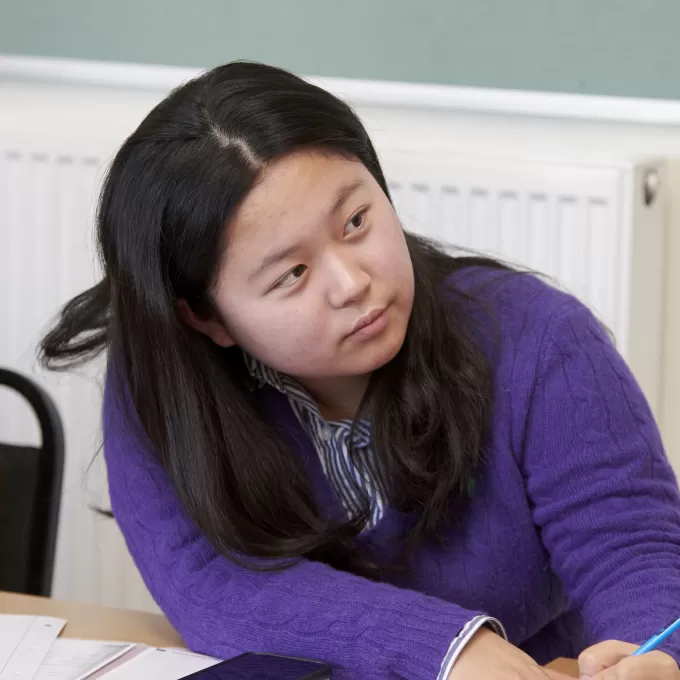 Seonyeong Hong from Republic of Korea looks up from her work in her general English class in Eastbourne. She has a smile on her face and she's wearing a lovely purple jumper.