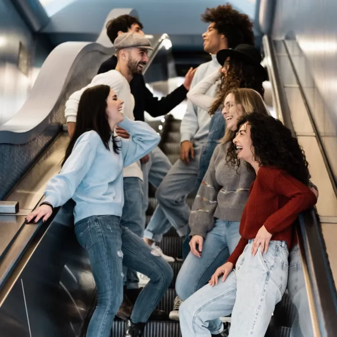 Seven students stand on both sides of the escalator chatting to each other. They clearly haven't been told about the rule where you have to stand on the right and pass on the left in London.