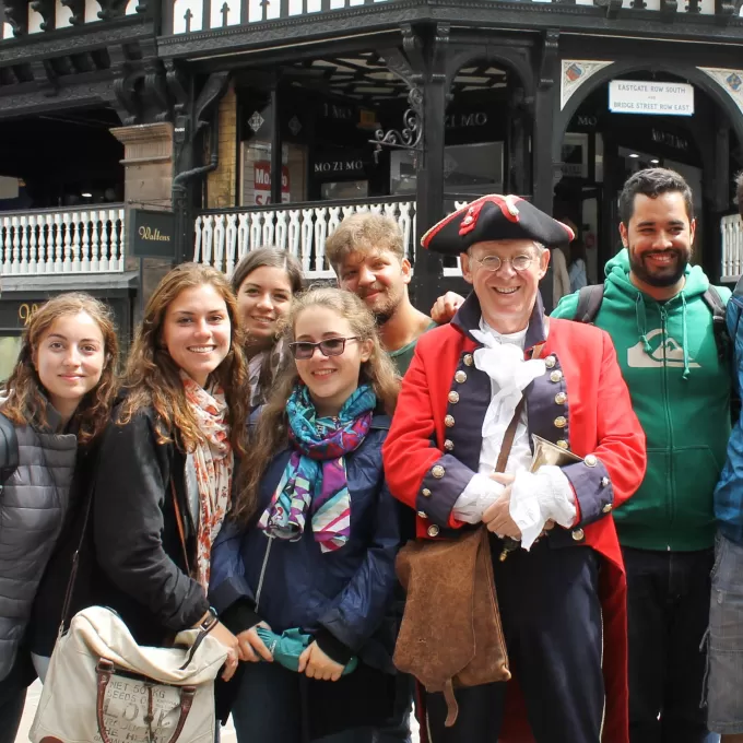 Teenage students from ELC Chester's summer course pose for a photograph with the local town crier. In olden days, they would have a bell and shout out what time it was as well as any breaking news. He's dressed in an official looking red and black jacket and he is wearing a tricorn hat.