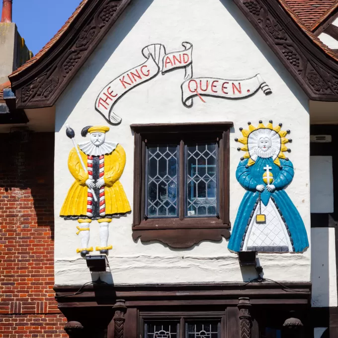 A photo of the upper facade of the King and Queen pub in Brighton, which shows very old looking wooden sculptures of a king and queen in relief against a tudor style gable roof.