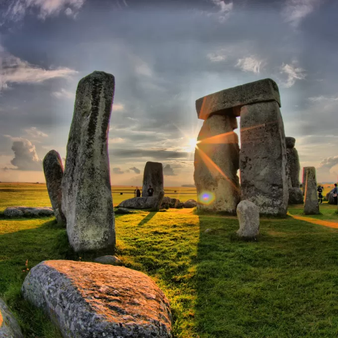One of the most famous sights in England - Stone Henge. In the photos we see some of the ancient standing stones just as the sun is shining out from round the side of one of them. The grass is green but dowsed in yellow light from the rising sun.