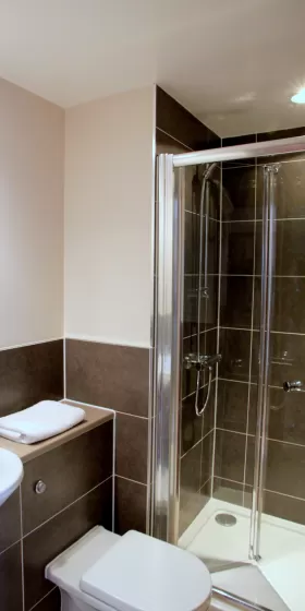 A photo of a bathroom with grey tiles and a shower cubicle, with white towels waiting to be used.