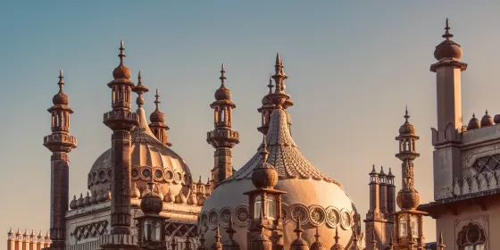 A stunning photo of the iconic Brighton Pavilion, more specifically the many towers and minarets that are slightly silhouetted against the background of the sky in the early morning.