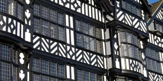 This photo shows some of the shop front above street level in Chester, set against a brilliant blue sky. The buildings have a tudor look to them, built from black timber beams filled with white plaster. The leaded windows are made up of hundreds of small rectangles of glass.
