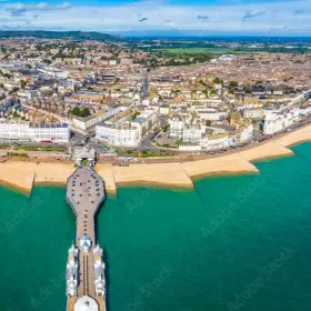 An aerial photo of Eastbourne's seafront, which uses a fish-eye lens to which makes it look like the beach is curving away from view. The pier is prominent in the shot, as is the sandy coloured beach. The sea is an inviting turquoise colour.