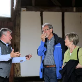 Two older students are standing in an ancient barn and are being given a guided tour.