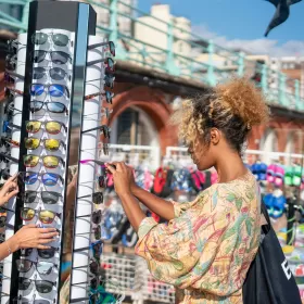 A photo of a sunglasses carousel where a couple of people are picking out a pair of new sunglasses, down on Brighton seafront.