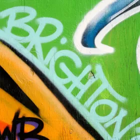 A close-up of graffiti in Brighton - we guess that becuase the word "Brighton" is visible in blue paint on a green, blue orange and black background.