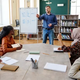 A library shot of a teacher who is teaching adult learners. They could be CELTA course trainees, but they could equally be students who have come along for practice lessons.